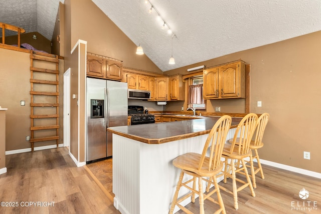 3021 N Arctic Fox Dr, Wasilla, AK 99654 - kitchen featuring appliances with stainless steel finishes, a textured ceiling, a peninsula, light wood-style floors, and a breakfast bar