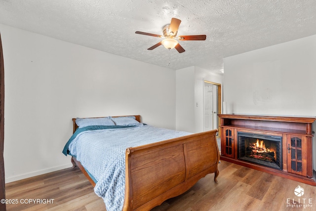 3021 N Arctic Fox Dr, Wasilla, AK 99654 - bedroom featuring wood finished floors, a textured ceiling, a lit fireplace, and ceiling fan