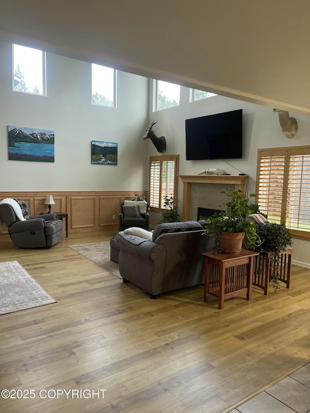 5693 Yukon Charlie Loop, Anchorage, AK 99502 - living room with a tile fireplace, plenty of natural light, light wood-type flooring, a towering ceiling, and a wainscoted wall