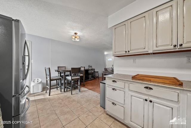 7200 Kiska Cir, Anchorage, AK 99504 - kitchen with stainless steel refrigerator with ice dispenser, light tile patterned floors, a textured ceiling, and cream cabinetry