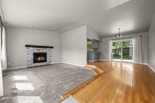 9645 Nulato Cir, Eagle River, AK 99577 - unfurnished living room featuring a chandelier, a stone fireplace, hardwood / wood-style floors, a textured ceiling, and vaulted ceiling