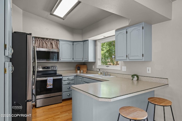 9645 Nulato Cir, Eagle River, AK 99577 - kitchen featuring appliances with stainless steel finishes, a peninsula, a kitchen breakfast bar, light countertops, and light wood-style floors