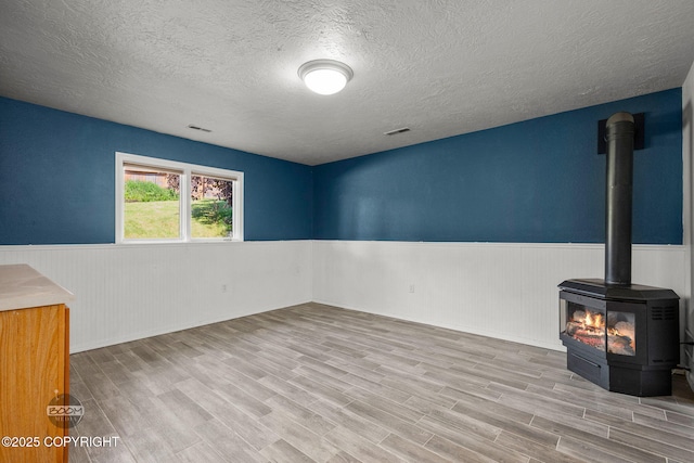 9645 Nulato Cir, Eagle River, AK 99577 - unfurnished room with a wainscoted wall, a textured ceiling, a wood stove, and wood finished floors