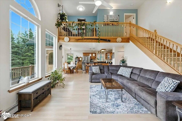 48350 Lakeside Ave, Soldotna, AK 99669 - living room featuring a ceiling fan, light wood-style floors, a towering ceiling, stairway, and a baseboard radiator