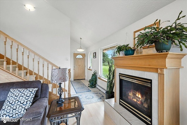 48350 Lakeside Ave, Soldotna, AK 99669 - living room with a baseboard heating unit, vaulted ceiling, light wood-style floors, a tile fireplace, and stairs