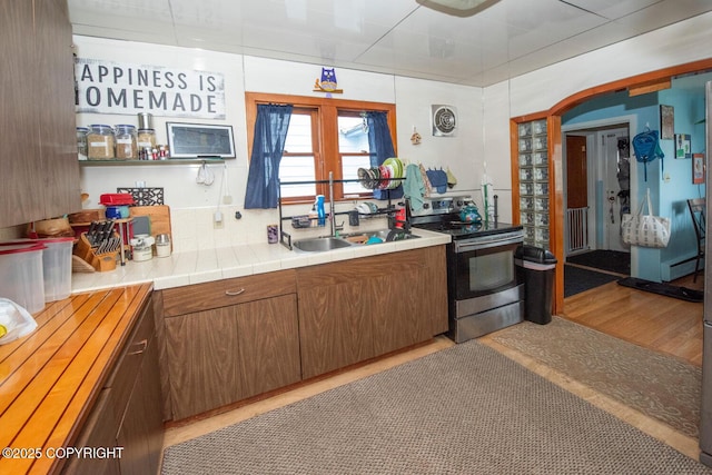 318 W 10th Ave, Anchorage, AK 99501 - kitchen featuring electric stove, light wood-style floors, baseboard heating, brown cabinetry, and arched walkways