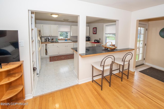 326 W 10th Ave, Anchorage, AK 99501 - kitchen with a kitchen bar, white cabinetry, white fridge with ice dispenser, a peninsula, and light wood-style flooring