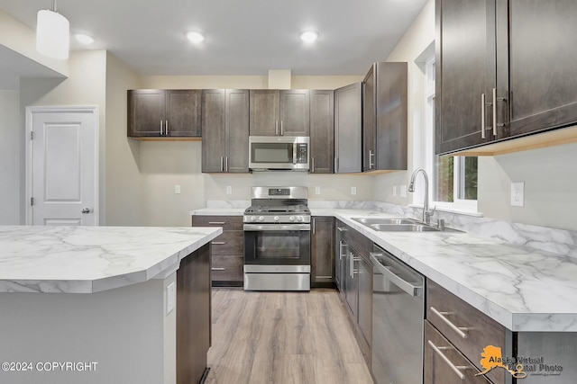 12229 Vista Ridge Loop, Eagle River, AK 99577 - kitchen featuring appliances with stainless steel finishes, dark brown cabinets, light wood-style flooring, decorative light fixtures, and light stone countertops
