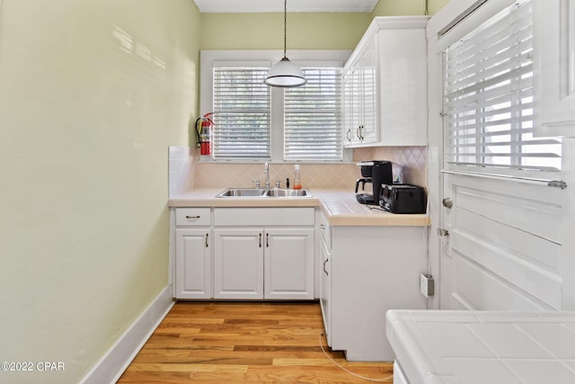 kitchen with tile counters, pendant lighting, sink, backsplash, and light hardwood / wood-style floors