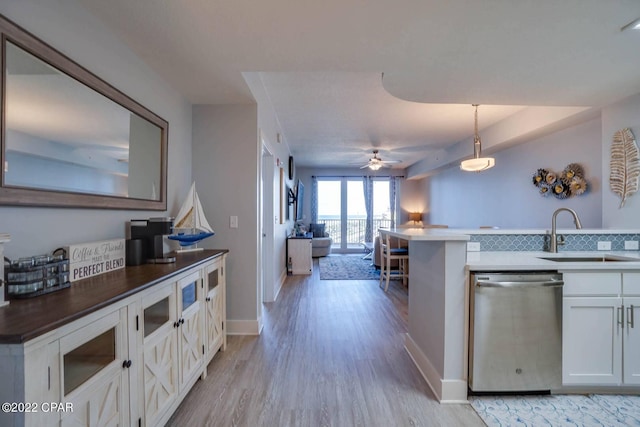 kitchen with a sink, white cabinetry, stainless steel dishwasher, light wood finished floors, and decorative light fixtures