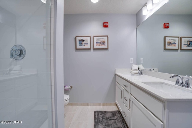 bathroom featuring a tile shower, double vanity, a sink, and toilet