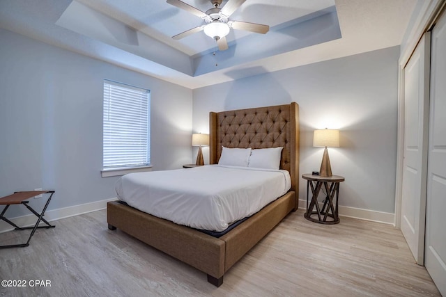 bedroom featuring baseboards, a ceiling fan, wood finished floors, a tray ceiling, and a closet