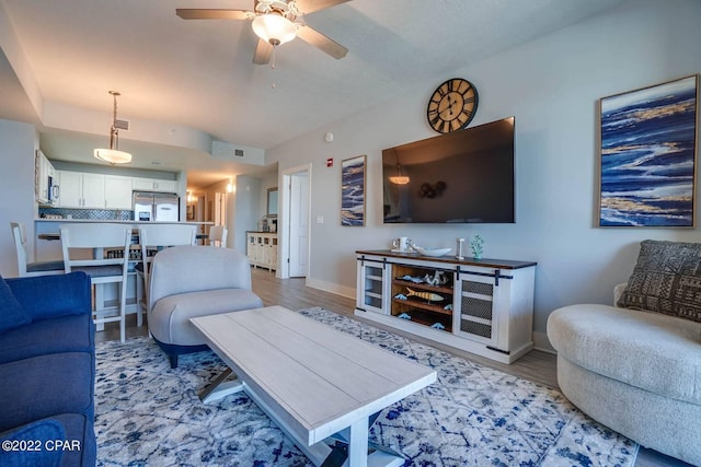 living room featuring baseboards, a ceiling fan, and light wood-style floors