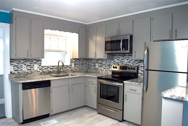 kitchen with gray cabinetry, light stone countertops, stainless steel appliances, and sink