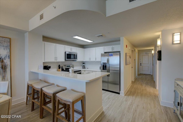 kitchen with backsplash, a kitchen bar, light wood-type flooring, stainless steel appliances, and white cabinets