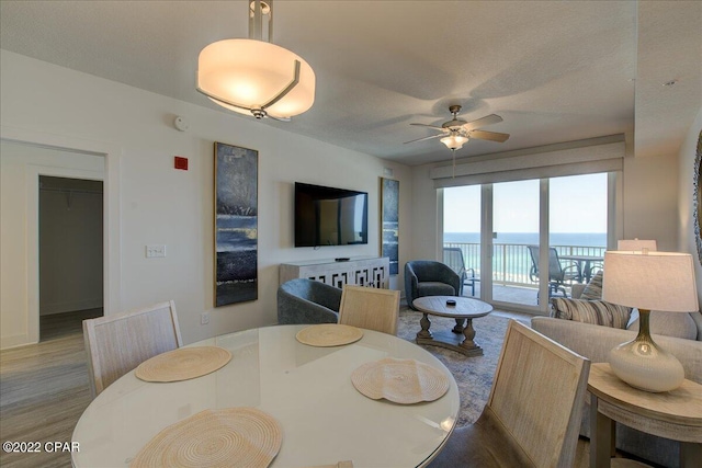 dining space with a textured ceiling, ceiling fan, hardwood / wood-style flooring, and a water view