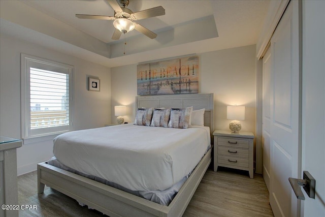 bedroom featuring a closet, a raised ceiling, hardwood / wood-style floors, and ceiling fan