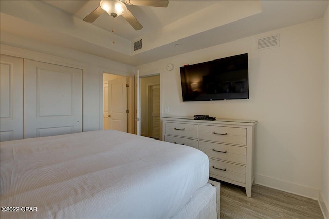 bedroom featuring a raised ceiling, light hardwood / wood-style floors, a closet, and ceiling fan