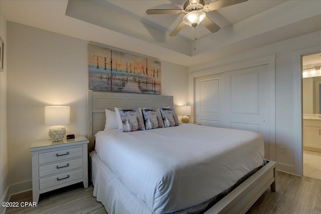 bedroom with connected bathroom, ceiling fan, a closet, wood-type flooring, and a raised ceiling