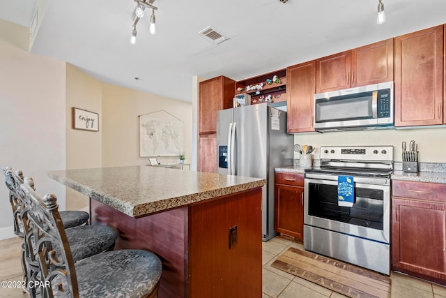 kitchen with light tile flooring, stainless steel appliances, a kitchen island, and a breakfast bar area