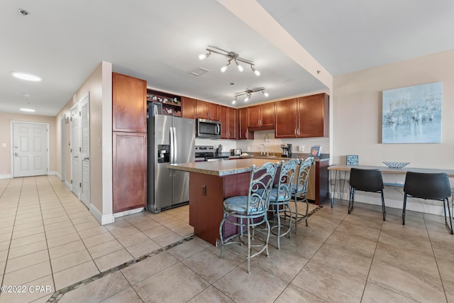 kitchen with sink, light tile floors, rail lighting, appliances with stainless steel finishes, and a breakfast bar