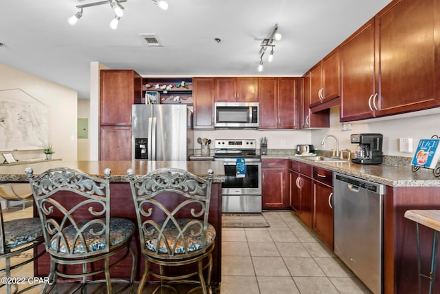 kitchen featuring stainless steel appliances, a kitchen island, light tile flooring, track lighting, and sink