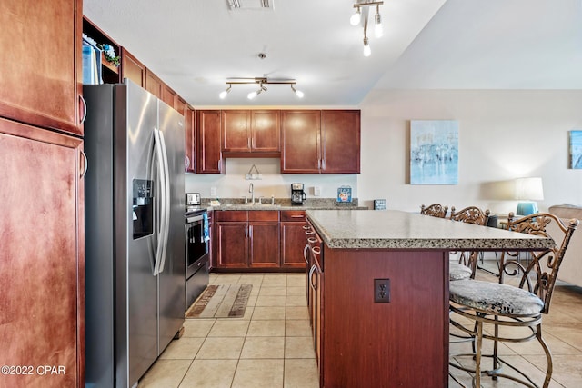 kitchen featuring light tile floors, stainless steel fridge with ice dispenser, a kitchen island, a breakfast bar, and track lighting