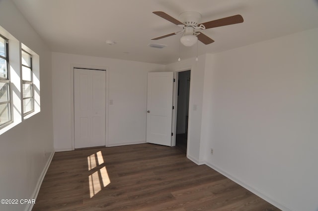 unfurnished bedroom with a closet, ceiling fan, dark wood-type flooring, and multiple windows