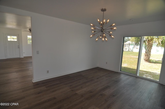 empty room with ceiling fan with notable chandelier, dark wood-type flooring, and a wealth of natural light