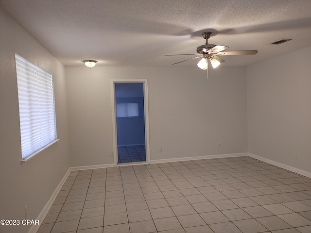 empty room with a textured ceiling, light tile flooring, and ceiling fan