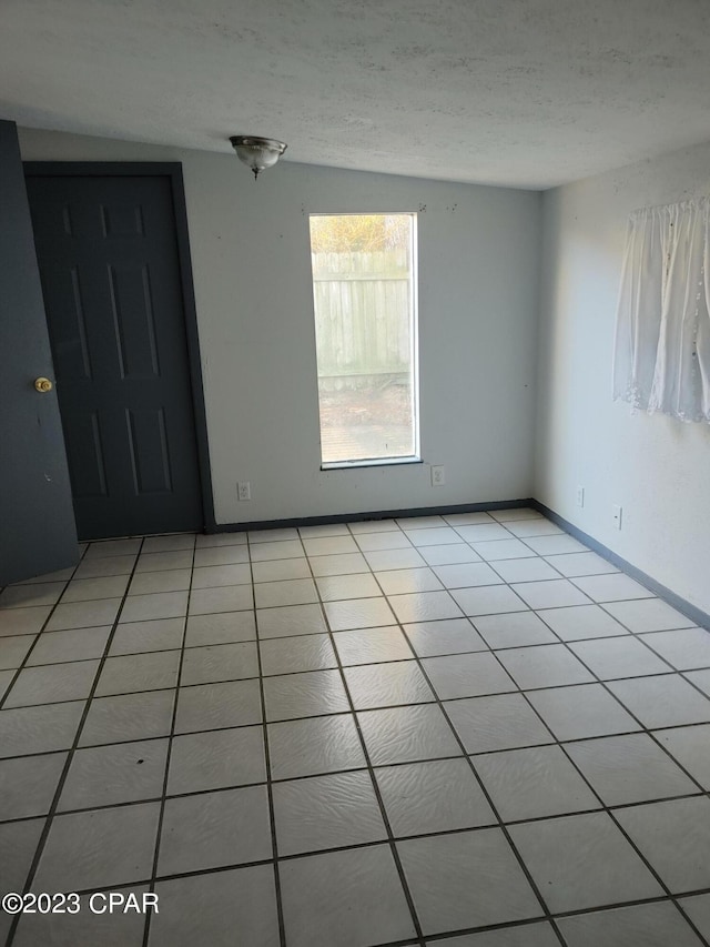 tiled empty room with a textured ceiling and lofted ceiling