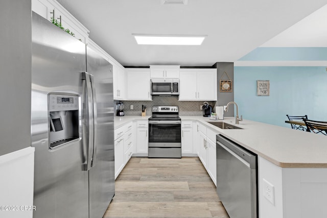 kitchen featuring light hardwood / wood-style floors, stainless steel appliances, sink, kitchen peninsula, and white cabinetry