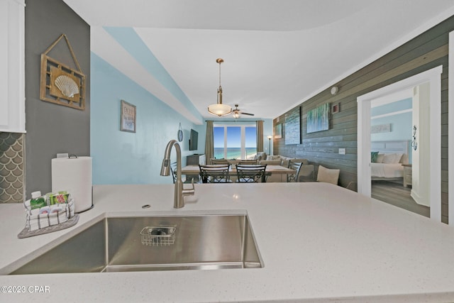 kitchen with wood walls, ceiling fan, hanging light fixtures, and sink