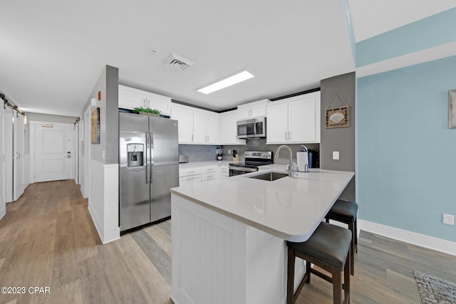 kitchen featuring light wood-type flooring, stainless steel appliances, white cabinetry, sink, and kitchen peninsula