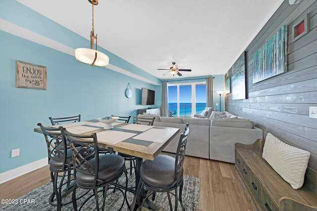 dining room with hardwood / wood-style flooring, ceiling fan, and wooden walls