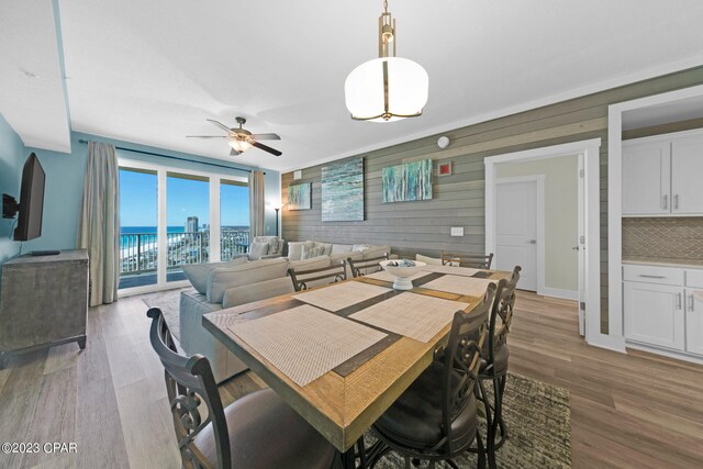 dining area featuring a water view, ceiling fan, wooden walls, and light hardwood / wood-style flooring