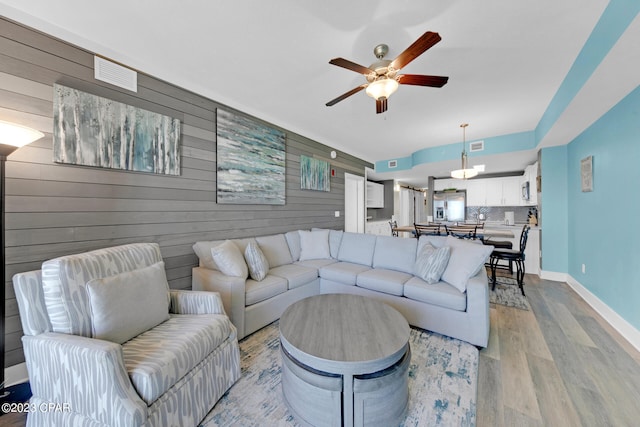 living room featuring ceiling fan, wooden walls, and light hardwood / wood-style flooring