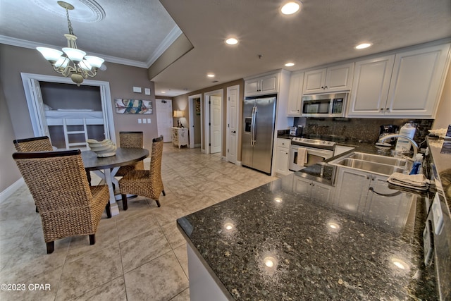 kitchen with an inviting chandelier, sink, stainless steel appliances, dark stone countertops, and white cabinets