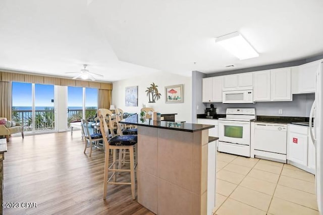 kitchen featuring light tile flooring, a kitchen bar, ceiling fan, white appliances, and white cabinetry