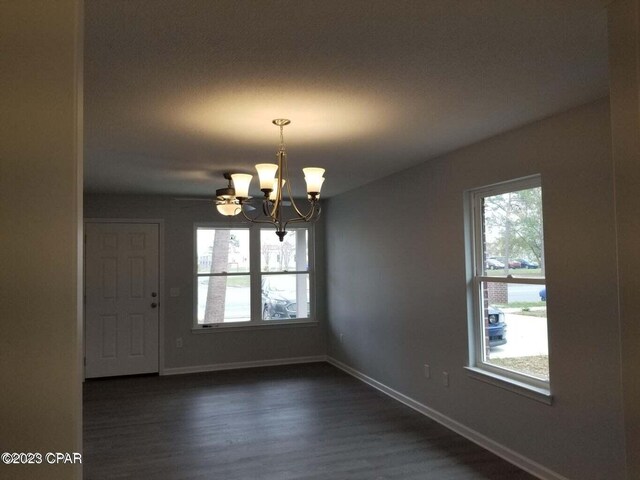 unfurnished room featuring a chandelier, plenty of natural light, and dark wood-type flooring