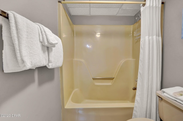 bathroom with a paneled ceiling, shower / bath combination with curtain, and toilet