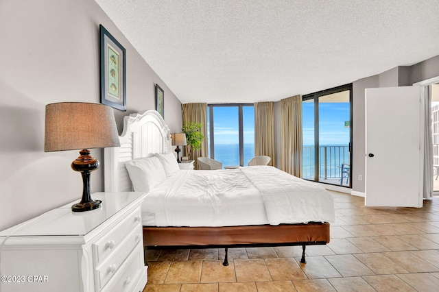 bedroom featuring a water view, light tile floors, access to outside, a textured ceiling, and floor to ceiling windows