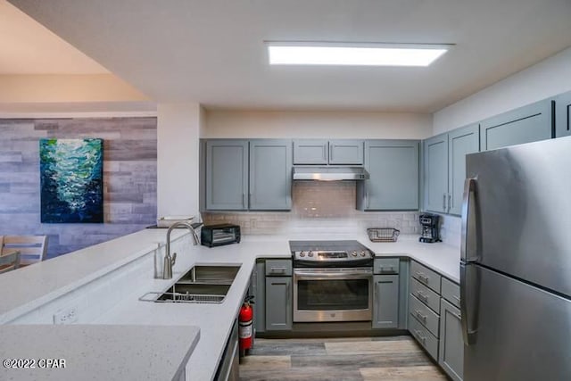 kitchen featuring light stone counters, stainless steel appliances, light hardwood / wood-style floors, sink, and kitchen peninsula