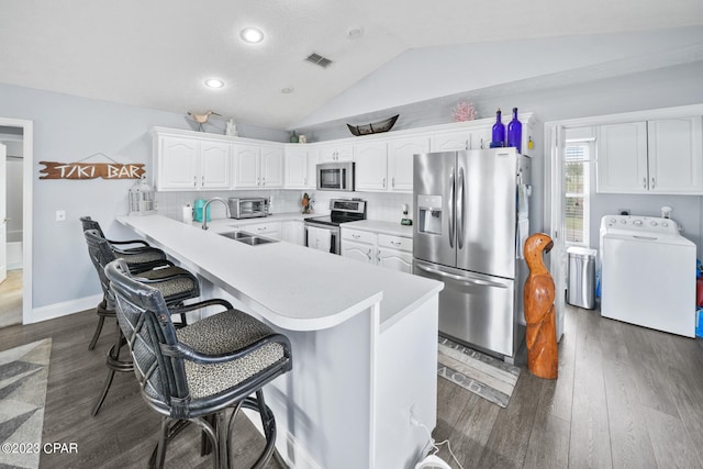 kitchen with stainless steel appliances, a breakfast bar area, washer / dryer, lofted ceiling, and dark hardwood / wood-style floors