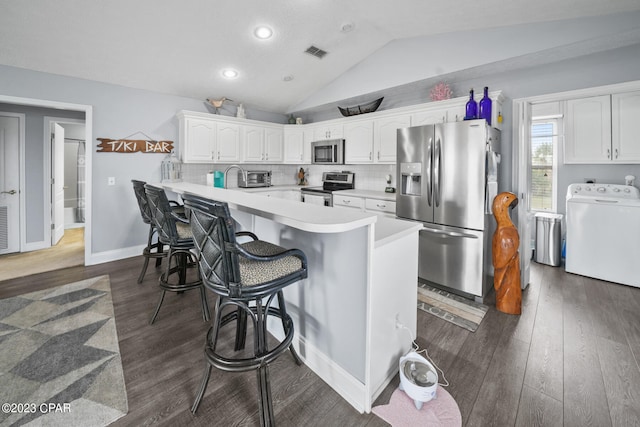 kitchen with stainless steel appliances, dark wood-type flooring, washer / clothes dryer, a breakfast bar area, and lofted ceiling