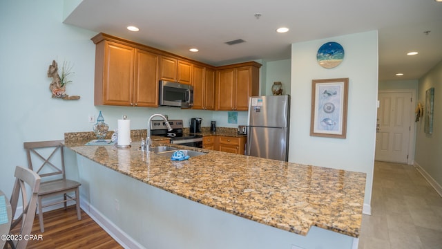 kitchen with kitchen peninsula, appliances with stainless steel finishes, light stone counters, light wood-type flooring, and sink