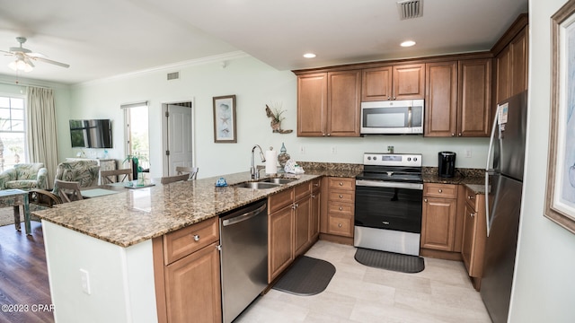 kitchen featuring stainless steel appliances, ceiling fan, crown molding, dark stone countertops, and sink