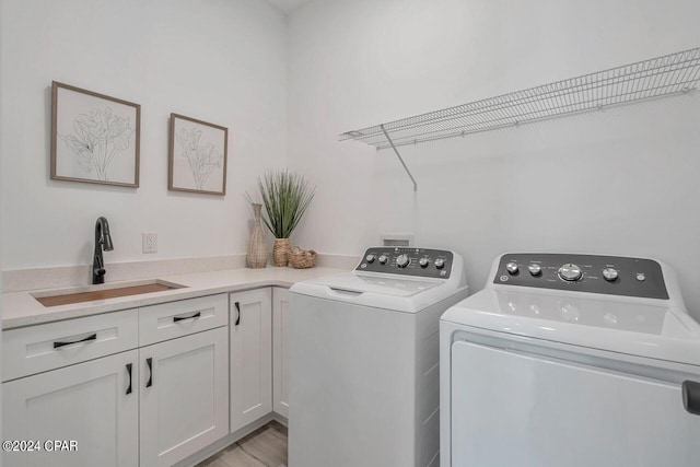 clothes washing area featuring cabinets, sink, washing machine and dryer, and light hardwood / wood-style flooring