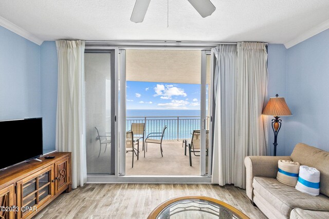 living room featuring light wood-type flooring, a textured ceiling, a water view, ceiling fan, and ornamental molding