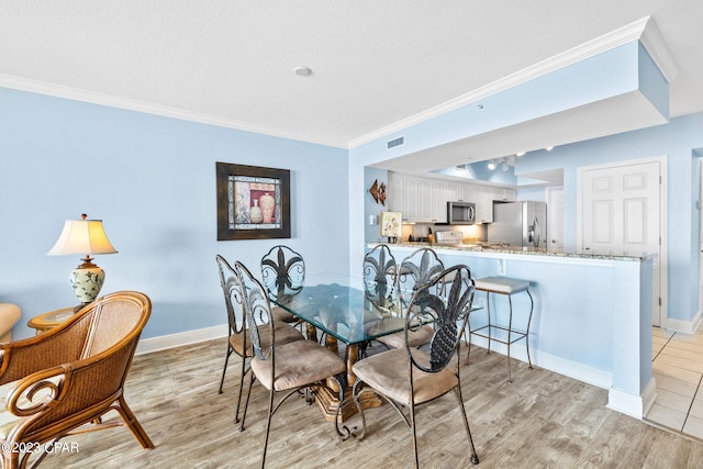 dining space featuring baseboards, visible vents, light wood finished floors, and ornamental molding